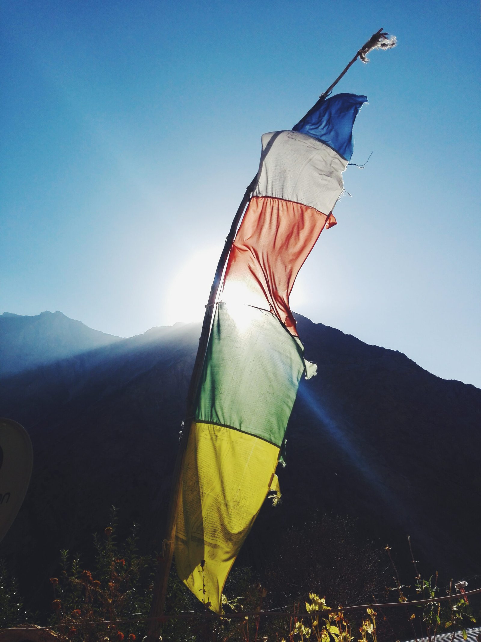 A single Tibetan prayer flag waving in the sun against a mountain