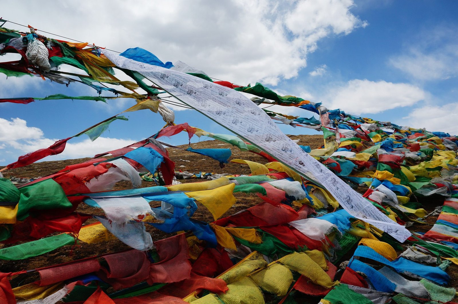 Hundreds of red, yellow, green, blue and white prayer flags heaped over a mountain pass under a blue sky with white clouds