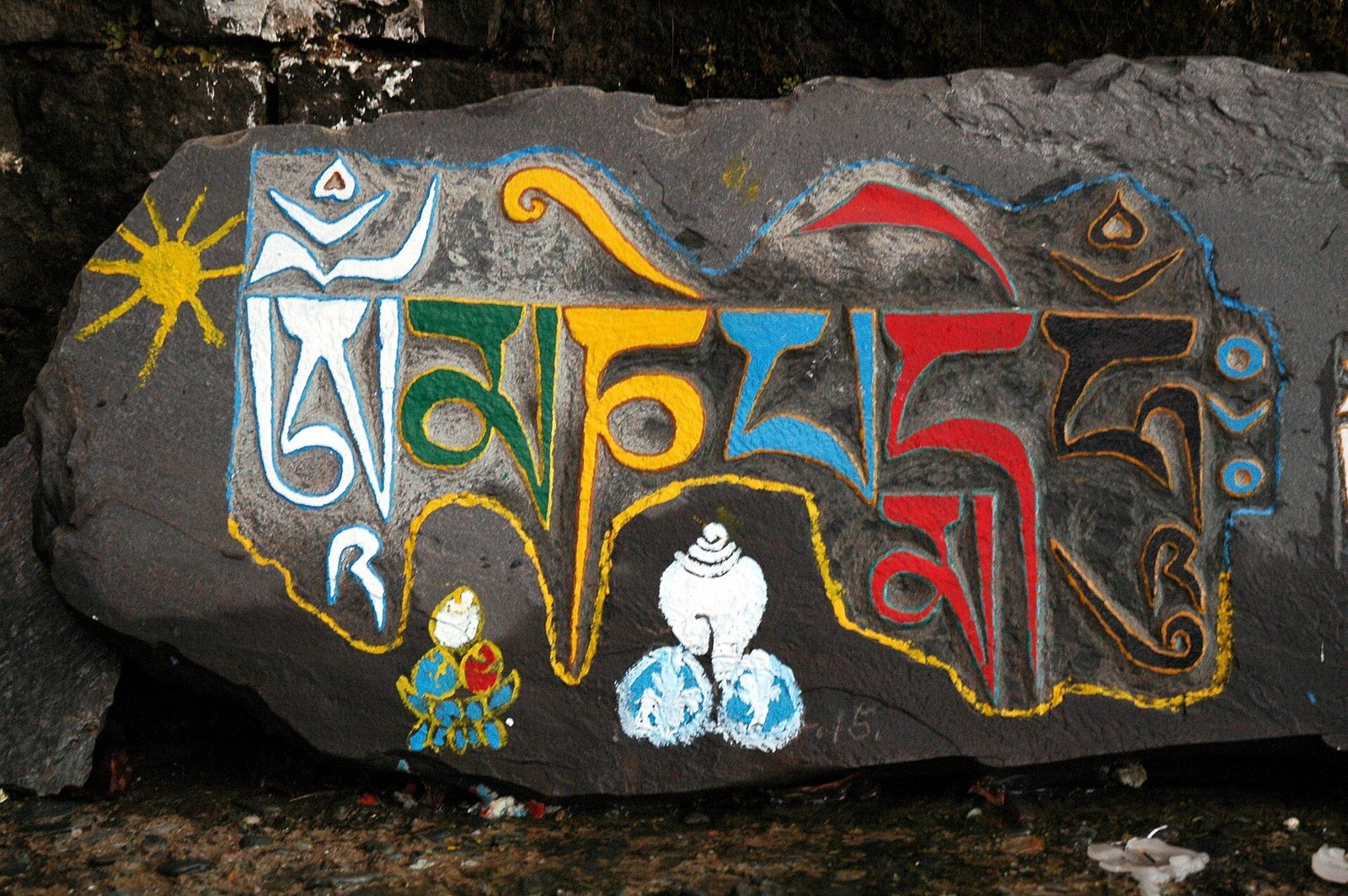 A dark stone painted with large colourful Tibetan letters