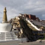 The white and red Potala Palace on its hill in Lhasa, with a white chorten in the foreground and a street below