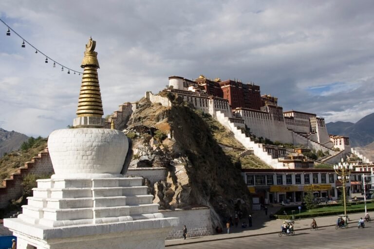 The white and red Potala Palace on its hill in Lhasa, with a white chorten in the foreground and a street below