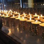 Rows of small lit butter lamps glowing in a dim room