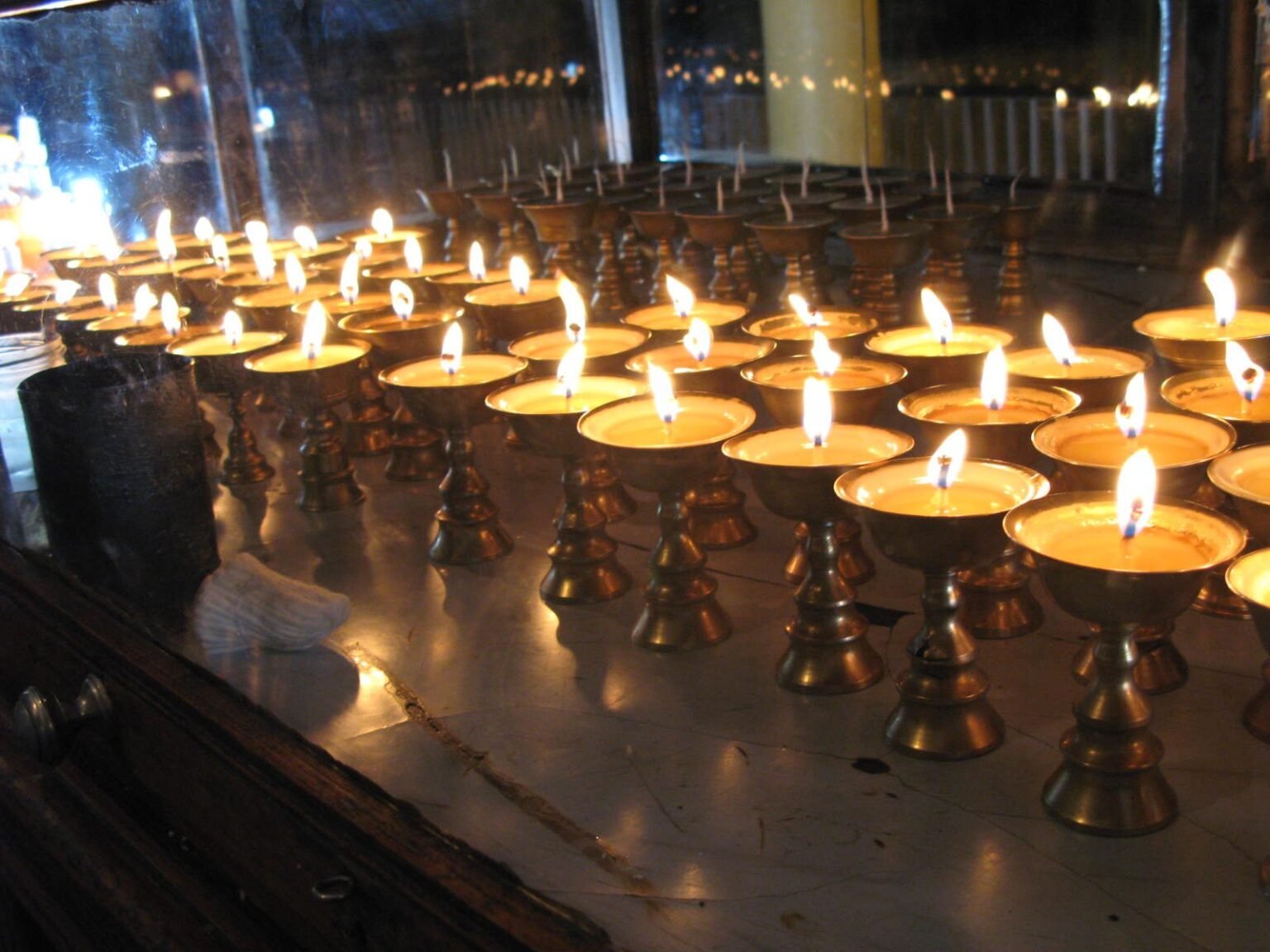 Rows of small lit butter lamps glowing in a dim room