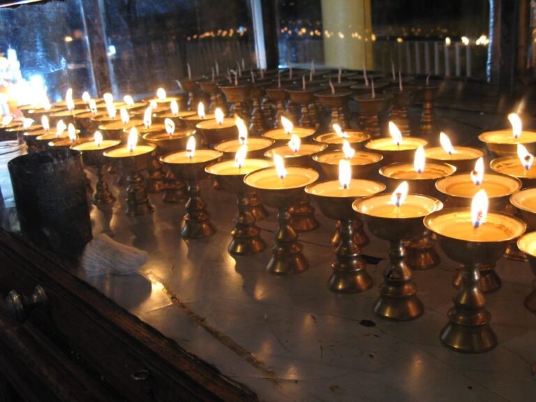 Rows of small lit butter lamps glowing in a dim room