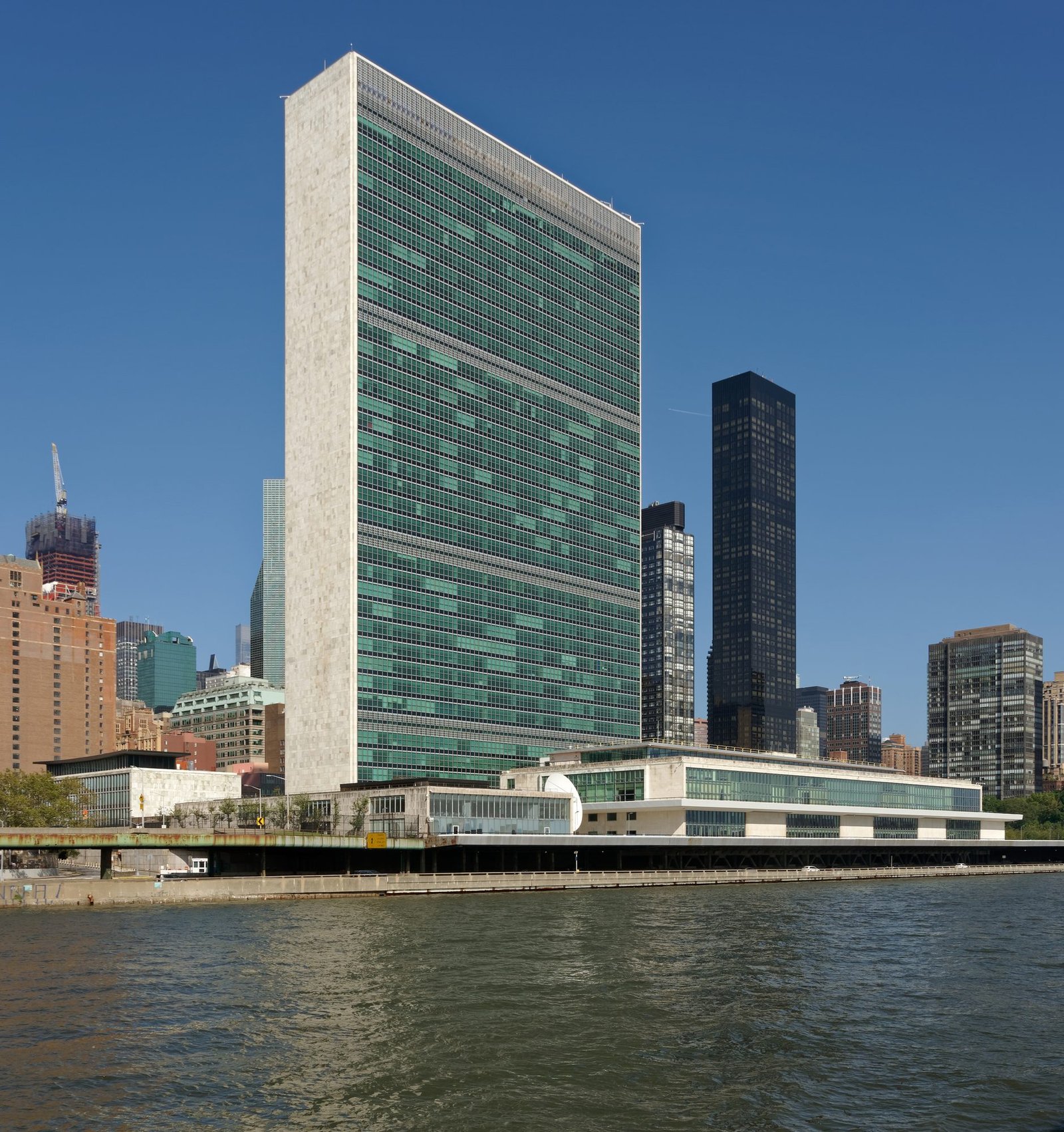 The tall glass and marble Secretariat tower of the United Nations headquarters beside the East River under a clear blue sky