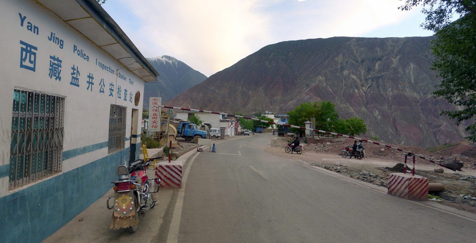 A roadside police checkpoint building with a blue sign in Chinese and English beside a mountain road