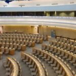A large circular United Nations assembly hall with curved rows of empty delegates’ desks