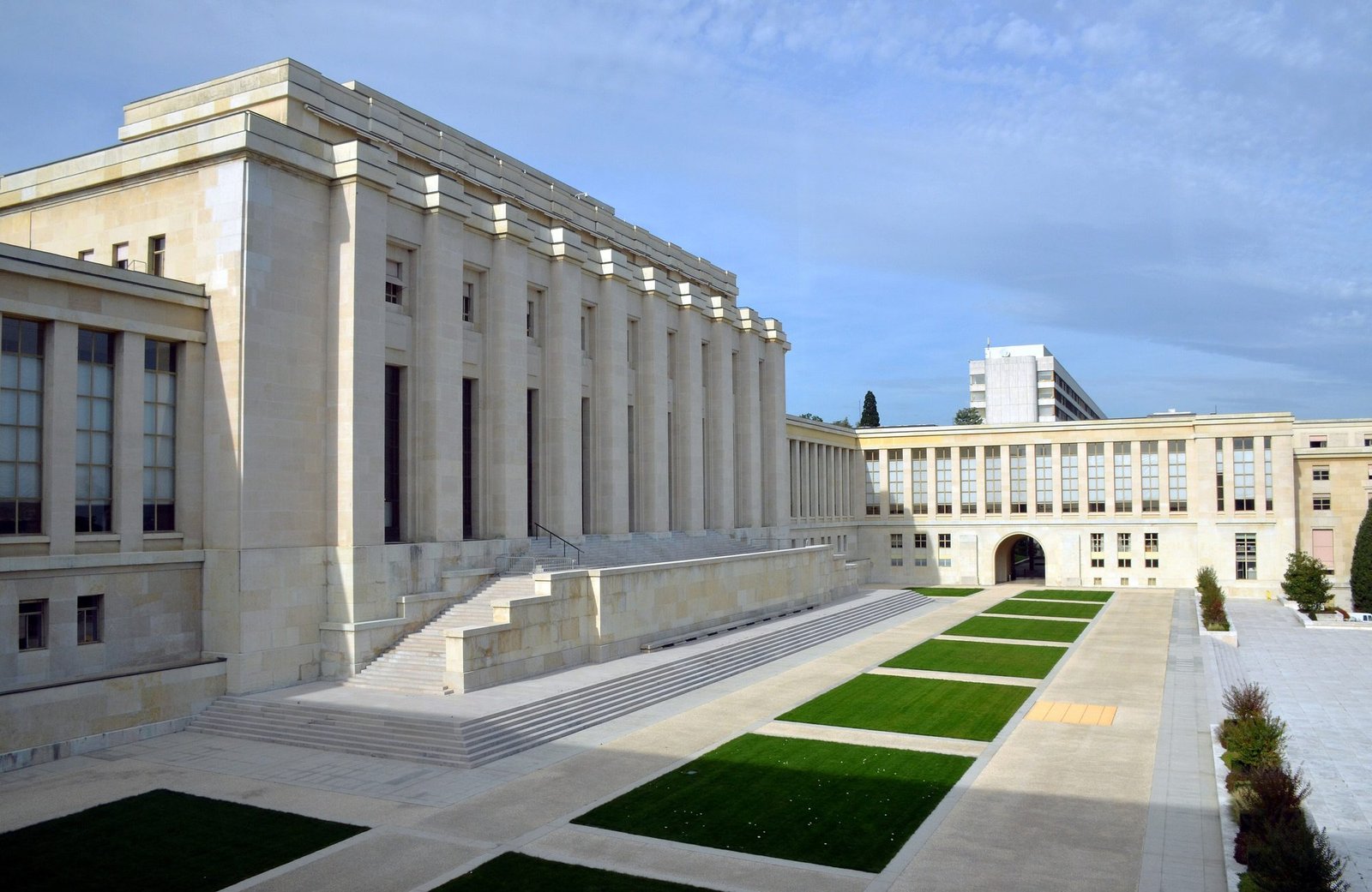 The pale stone colonnade of the Palais des Nations with wide steps and strips of lawn