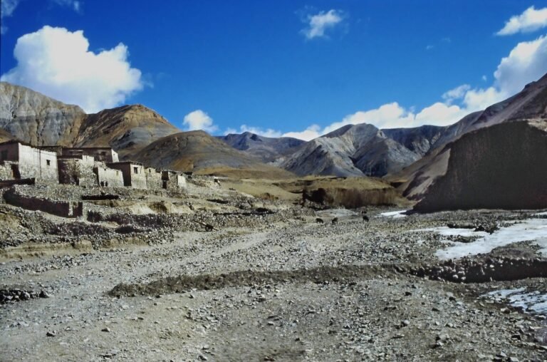 Whitewashed village houses at the foot of bare mountains beside a stony riverbed