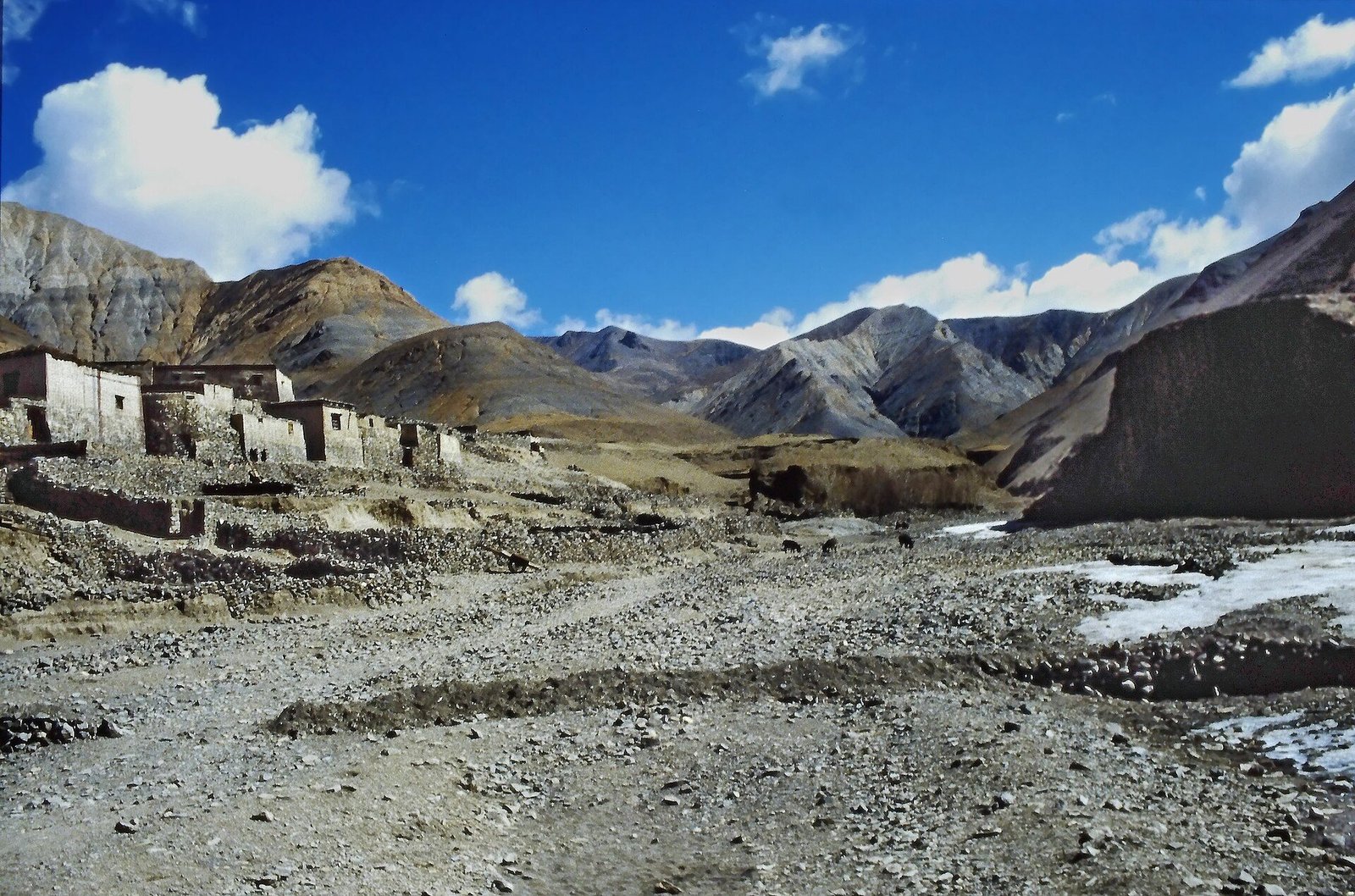 Whitewashed village houses at the foot of bare mountains beside a stony riverbed