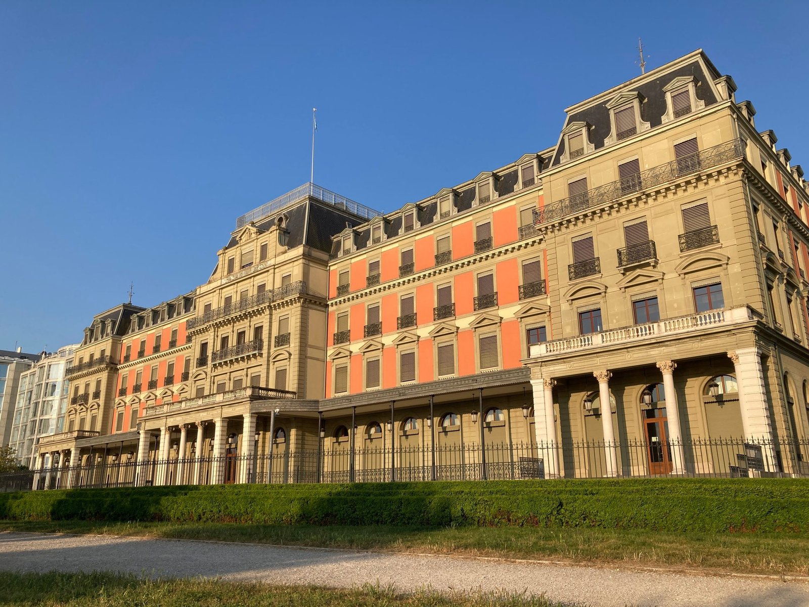 A large 19th-century building with a pink and cream stone facade behind a lawn and railings