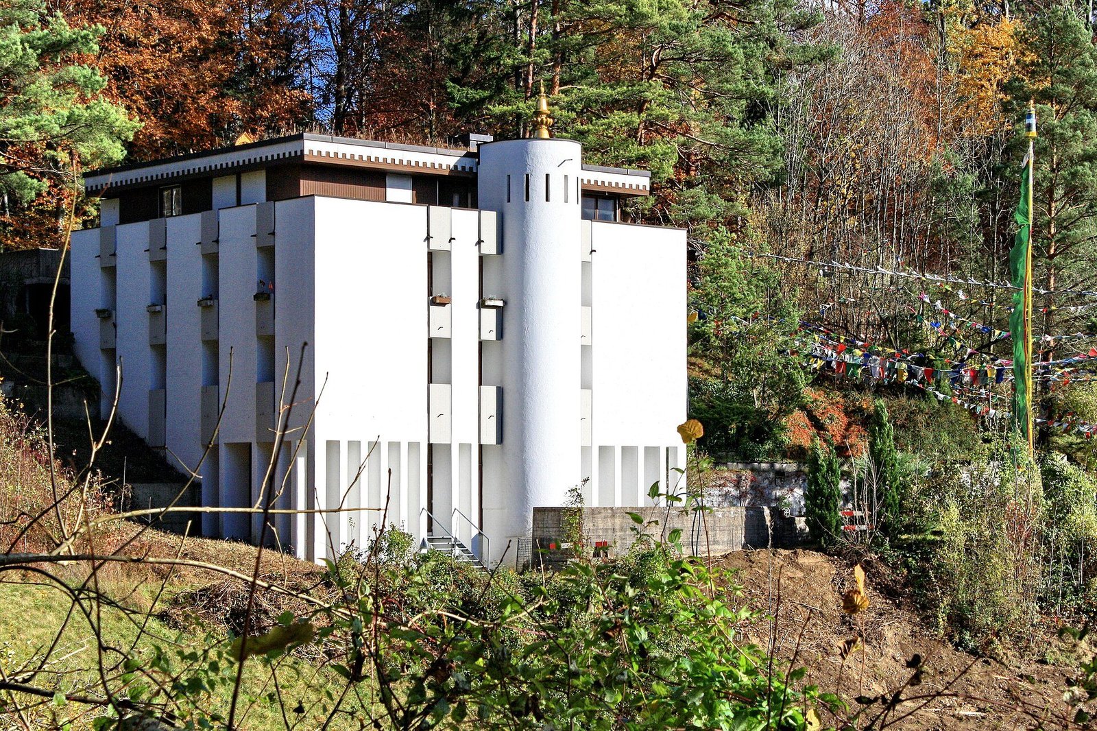 A white modernist monastery building with a round tower among autumn trees