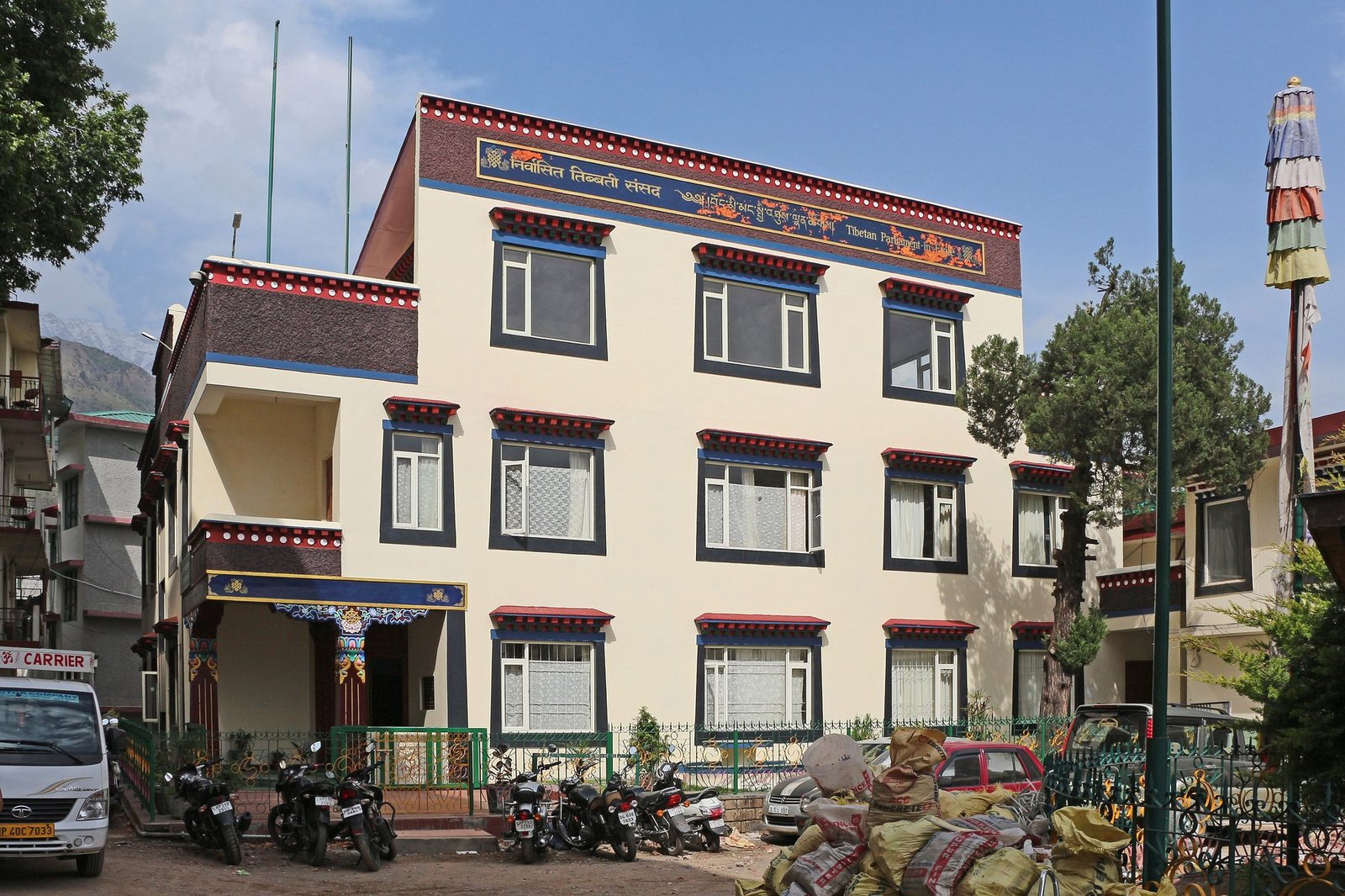 A white three-storey building with Tibetan-style painted window frames and a sign in Tibetan and English