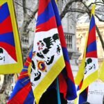 Several Tibetan snow lion flags held up in front of bare trees and Paris buildings