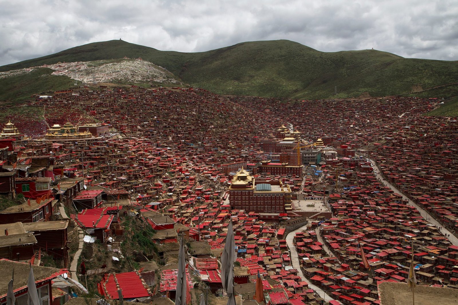 Thousands of small red wooden houses filling a valley around golden-roofed temples, green hills behind