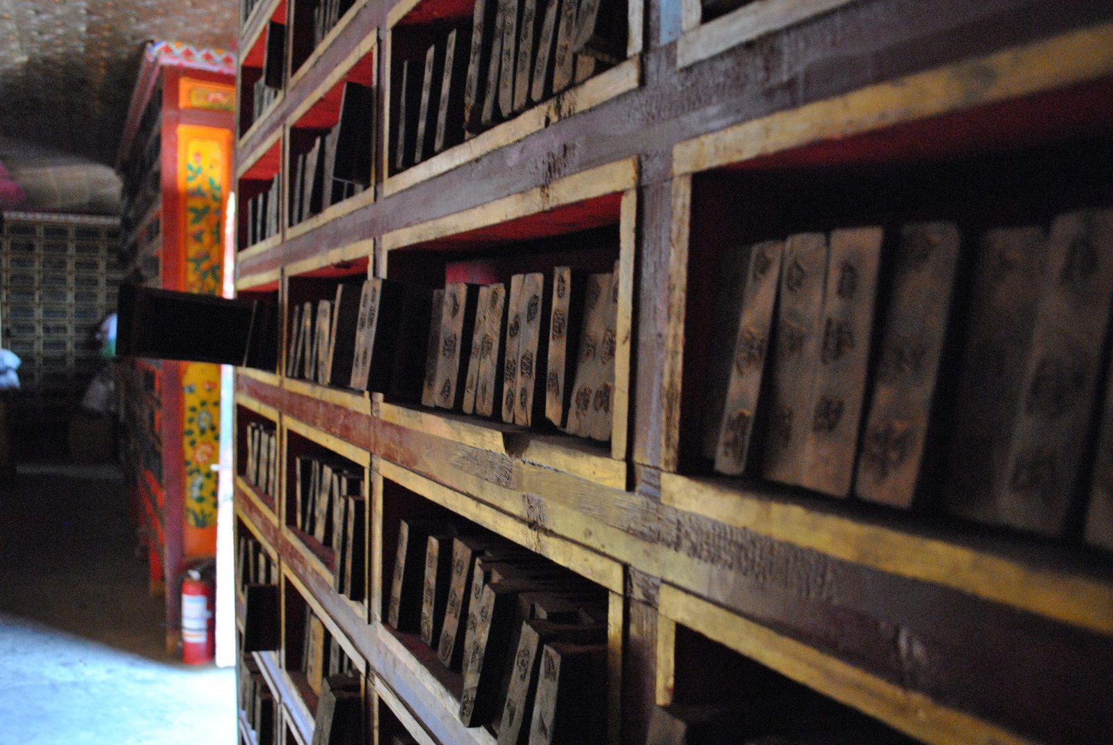 Wooden shelves with rows of carved printing blocks, a painted pillar on the left
